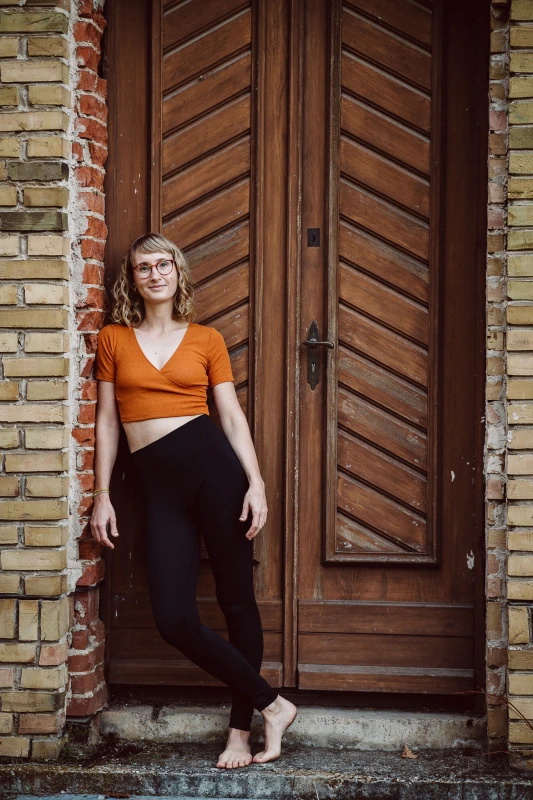 Marie Rohde von vispharana yoga lehnt entspannt lächelnd im Park Babelsberg in Potsdam an einer Tür.