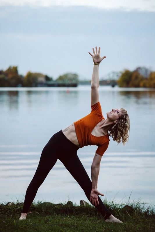 Marie Rohde von vispharana yoga praktiziert mutig und achtsam die Yogaübung Trikonasana im Park Babelsberg in Potsdam.